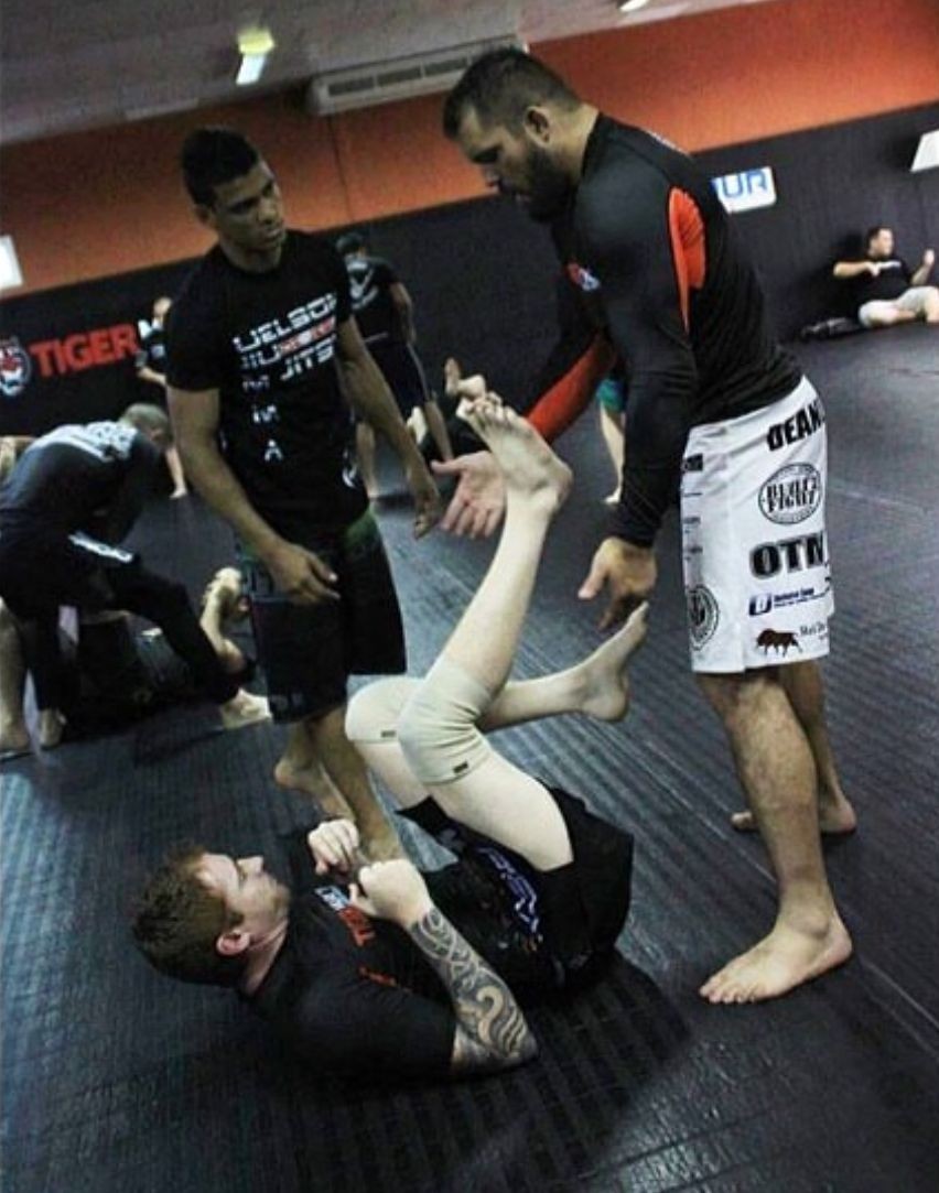 Mixed martial arts training session with participants practicing ground techniques on a padded mat in a gym.